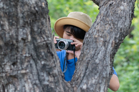 Asian boy taking photo with old camera on tree in the park.