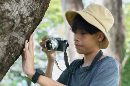 A young photographer in a bucket hat taking a close-up shot of tree bark with a camera, showing interest in nature and texture.の写真素材