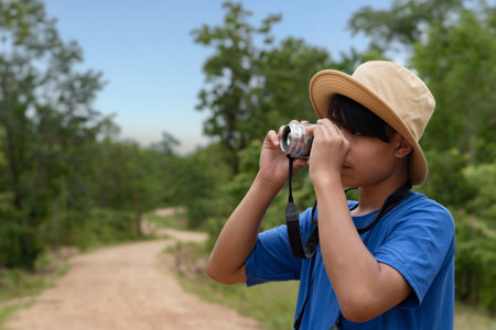 A young naturalist looks high into the treetops using his binoculars, with a wide expanse of green foliage filling the background.の写真素材