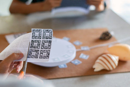 A person cuts out AR markers (ArUco codes) to prepare a white motorized turntable for smartphone...