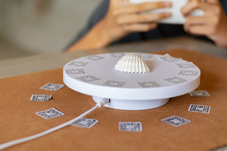 Person using a smartphone to capture a seashell on a photogrammetry 3D scanner, illustrating the...