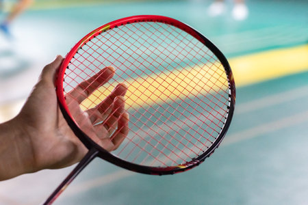 Badminton racket in hand, badminton court background.