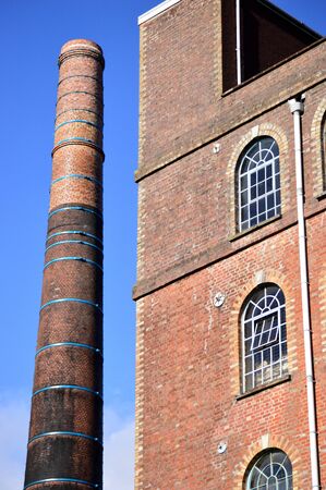 Factory with tall chimney alongside arched windows against a blue sky