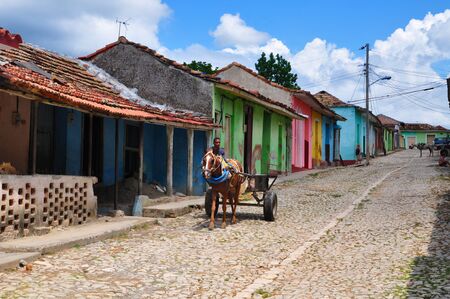 Trinidad, Cuba - August 13, 2015: Colourful street in Cuban boy rides on horse cart. Some people are standing or sitting in front of their houses.のeditorial素材