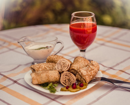 Tasty pancakes with meat on white plate closeup. Crepes stuffed with finely cut meat. glass of tomato juice and white sauce.の写真素材