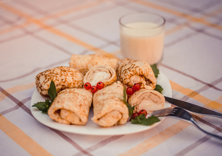 Tasty pancakes with home made cheese on white plate closeup. Crepes stuffed with cheese, and glass of milk on checked table cloth.の写真素材