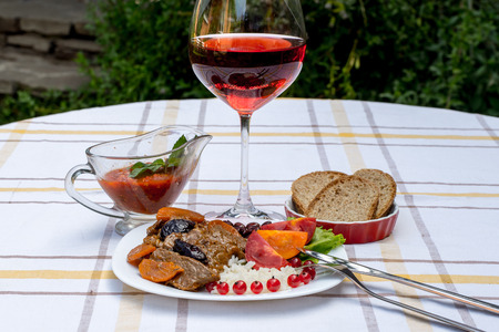 Beef stew with carrot and dried plum, topping with rice, beans and tomatoes. Served on a white plate with crusty bread, home made sauce and glass of red wine.の写真素材