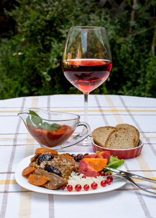 Beef stew with carrot and dried plum, topping with rice, beans and tomatoes. Served on a white plate with crusty bread, home made sauce and glass of red wine.の写真素材