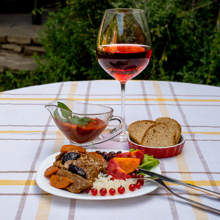 Beef stew with carrot and dried plum, topping with rice, beans and tomatoes. Served on a white plate with crusty bread, home made sauce and glass of red wine.の写真素材