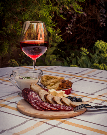Sliced smoked sausage, home-made sausage, soft cheese, home-made bread bread on the wood plate, glass of red wine and sauce.の写真素材