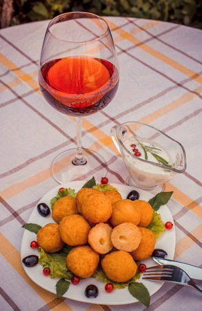 Hot juicy fried cheese balls with sauce on a white plate. Glass of red wine.の写真素材
