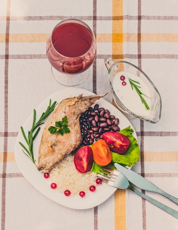 Gourmet roasted rabbit leg with rice and beans. White sauce and glass of tomato juice. Meal is served on white simply plate and checked table cloth, with cutlery. Health and light meal good for diet.の写真素材