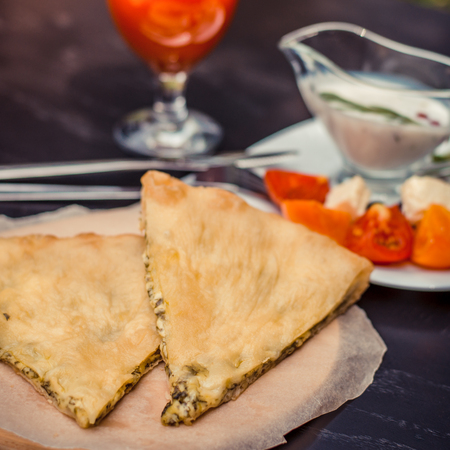 Delicious rustic crispy pie with cheese and herbs. Served on wooden plate, surrounded by glass of tomato juice, white sauce and vegetables. Caucasian, greek, mediterranean cuisine. Healthy diet    lunch, breakfast or snack.の写真素材