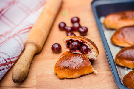 Oven fresh home made baked patties stuffed with cherry. Delicious pastries on a baking sheet, surrounded by cherry, napkin and rolling pin.の写真素材