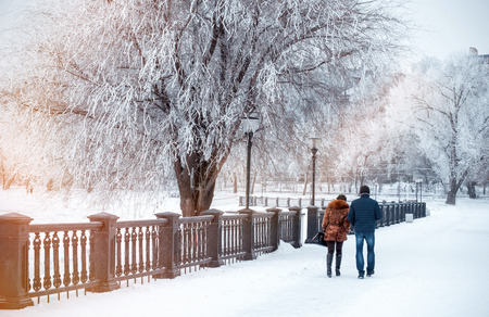 Girl and young man walk along snow-covered quay. Taganrog, Russia, January 7, 2017. Winter landscape of solid sea embankment with falling snowflakes, trees covered with snow, frosty branches.の写真素材