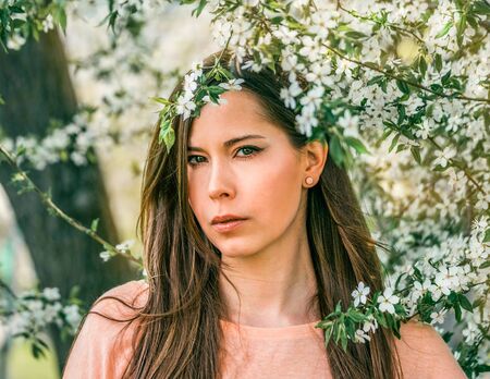Beautiful young brunette girl in a blooming cherry orchard. Happy smiling young woman with spring flowers at garden. Girl in the spring garden among the blossoming.の写真素材