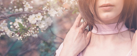 Beautiful girl with spring cherry flowers, sunshine backlit. Pretty young brunette woman's hand touching a blooming tree branches. Fashion, happiness and lifestyle concept.の写真素材