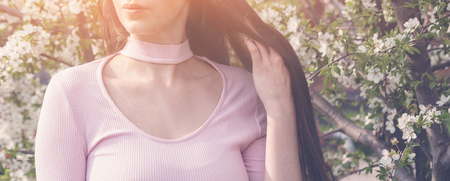 Beautiful girl with spring cherry flowers, sunshine backlit. Pretty young brunette woman's hand touching a blooming tree branches. Fashion, happiness and lifestyle concept.の写真素材