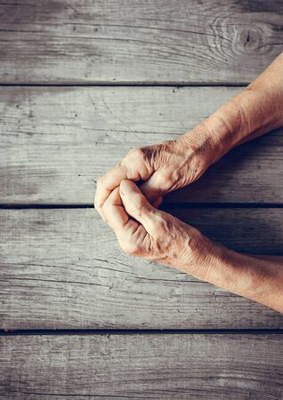 Elderly woman hands on rustic wooden background. Senior woman with fingers crossed. Wrinkled palms stretched forward. Religion, take care, mothers day, warmth concept. Human emotions, old people health, love and compassion.の写真素材