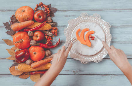 Autumn table setting, menu concept, hands with vintage fork, knife, sliced pumpkin. Thanksgiving healthy fresh food, top view, flat lay, copy space. Fallen leaves, fruits, vegetables, wooden table.の写真素材
