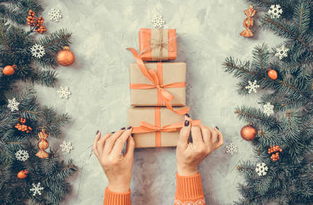 Christmas gray grunge background, fir twigs, berries, snowflakes, baubles, top view. Woman hands in red pullover hold craft gift boxes with ribbons. New Year decoration, pine tree branches, cones.の写真素材