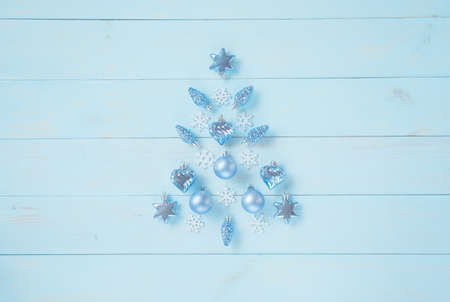 Christmas light blue background. Festive decoration with blue and silver baubles, hearts, snowflakes, stars, cones in Christmas tree shape arranged on rustic pastel blue wooden table, top view.の写真素材