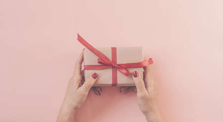 Woman hands holding gift with red ribbon on pink background, copy space. Flat lay, hands and present box, top view. Valentine or love, spring holidays, Christmas and birthday concept.の写真素材
