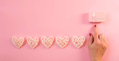 White wicker hearts line on pink background, copy space. Woman hand pointing finger pink gift box, top view. Valentine or love, spring holidays, Christmas and birthday concept.の写真素材