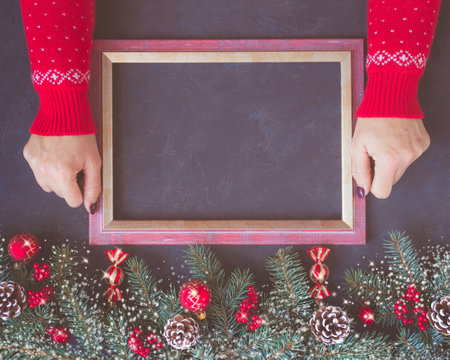 Christmas dark lilac grunge horizontal background, top view. Fir twigs, red golden berries, baubles, New Year decoration. Woman hands in patterned red sweater hold frame for wishes, copy-space.の写真素材