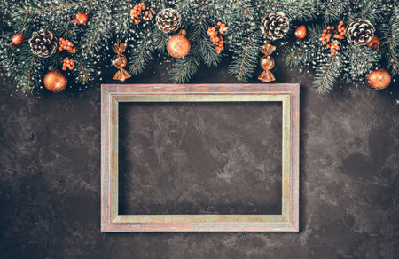 Christmas dark grunge horizontal background, top view. Fir twigs, red golden berries, baubles, frame for wishes. New Year decoration, pine tree branches, snow covered cones, copy space.の写真素材