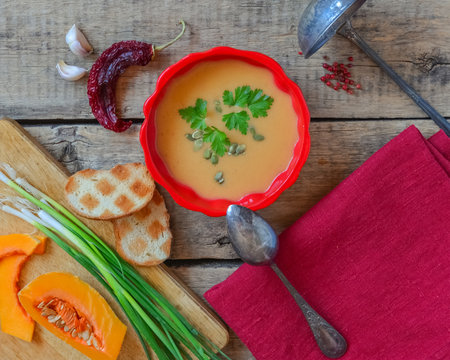 Pumpkin soup on wooden table, linen cloth, vintage cutlery. Autumn cream soup, seeds and parsley. Sliced herbs, pumpkin on cutting board, cooking process. Thanksgiving dinner, flat lay, top view.の写真素材