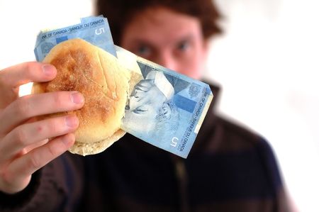 A young man holds up an english muffin with 5 dollar bills insideの写真素材
