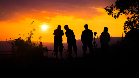 Silhouette of group of friends standing and watching sunset on mountain in evening.の写真素材