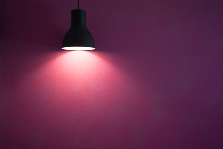 Red wall illuminated by vintage black stylish cone lamp.の写真素材