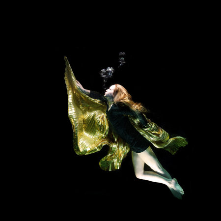 Young woman dancing in golden dress on black background.の写真素材