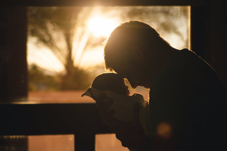 Silhouette of a father with his newborn baby on the windowsill