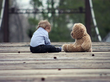 Little boy playing with a teddy bear on a wooden bridge.の写真素材