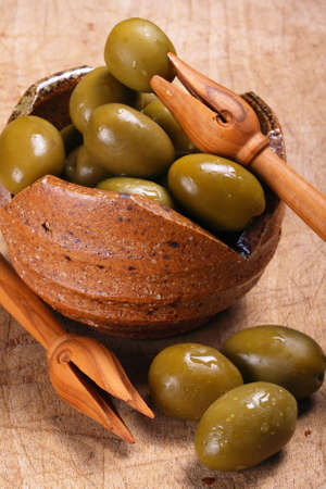 Green olives in a rustic ceramic bowl and olive wood pickersの写真素材