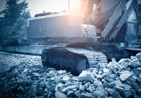 heavy organge excavator with shovel standing on hill with rocksの写真素材