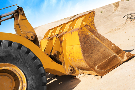 Yellow excavator on new construction site, with the bright sun and nice blue sky in the background