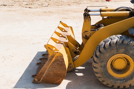 Yellow excavator on new construction site, with the bright sun and nice blue sky in the background