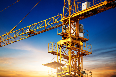 Industrial construction cranes and building silhouettes over sun at sunrise.の写真素材
