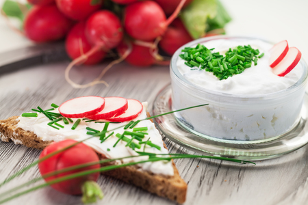 A bowl with curd and radish and a heart shaped chives decoration and brown breadの写真素材
