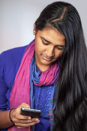 Young pretty india woman looking at her smartphone, vertical