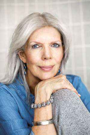 Attractive mature woman sitting with hand on knee looking at cameraの写真素材