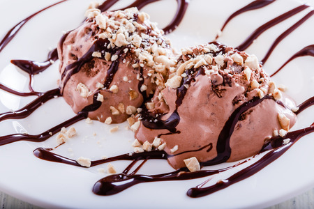 Chocolate ice cream with cashews and chocolate syrup on white tableの写真素材