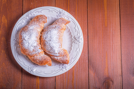 Two fresh croissant on a white plate on a wooden backgroundの写真素材