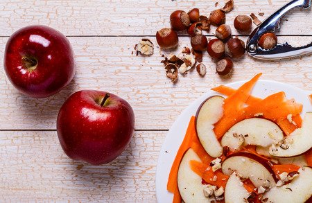 Fresh salad with apples, carrots, hazelnuts on a white wooden backgroundの写真素材
