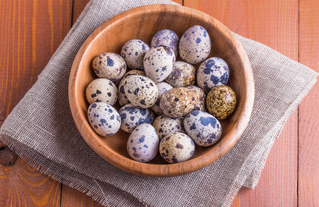 Quail eggs in a wooden bowl on a wooden tableの写真素材