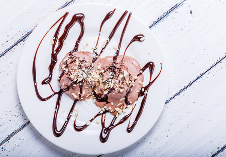Chocolate ice cream with cashews and chocolate syrup on white tableの写真素材